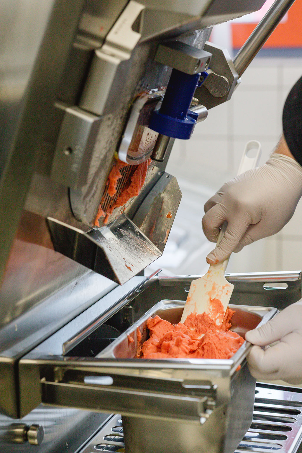 Behandschuhte Hände füllen rotes Sorbet mit einem Spatel aus einer Maschine in eine Metallform.