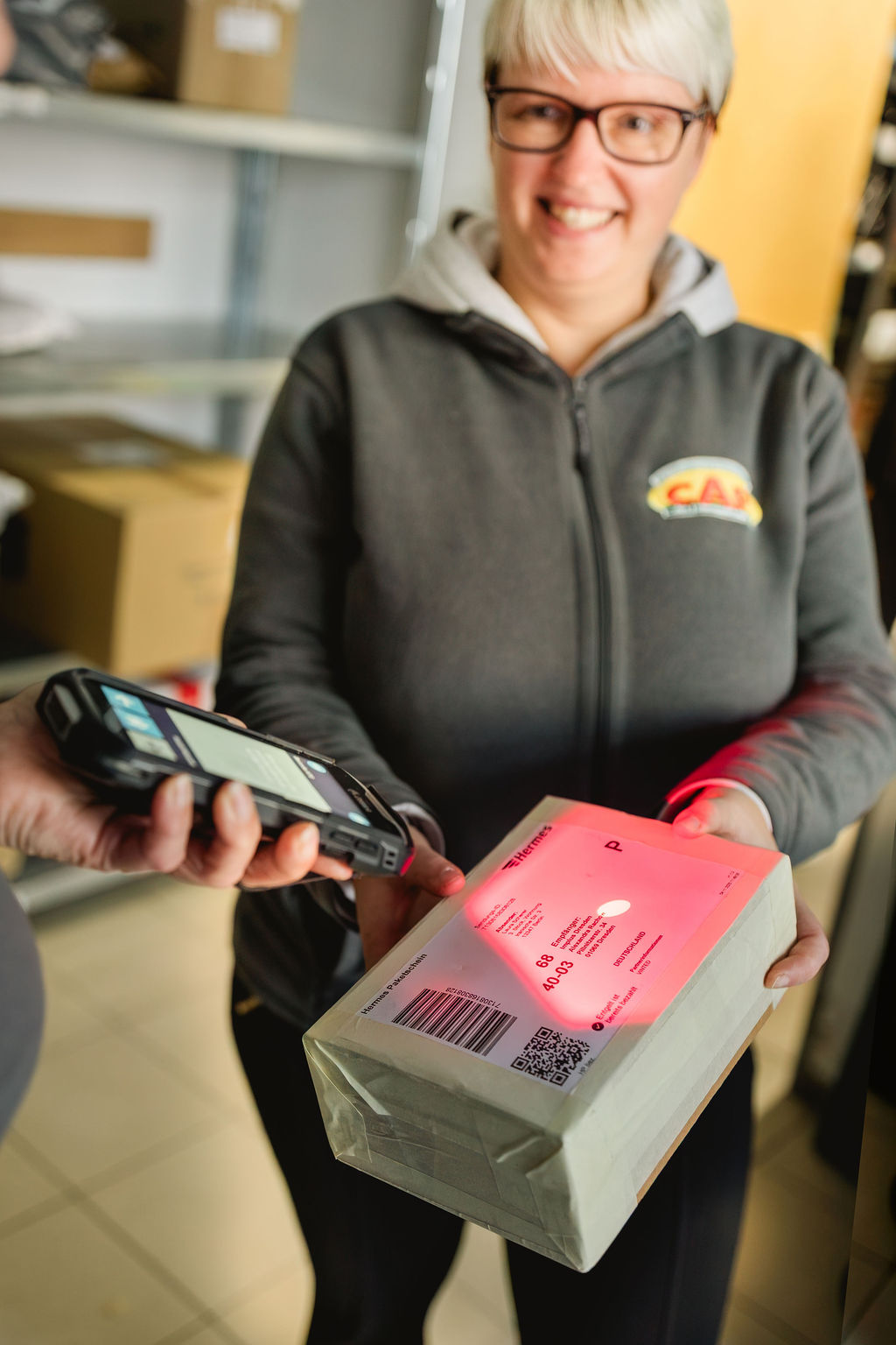 Eine Frau mit weißem Kurzhaar lässt ein Hermes-Paket mit einem Handscanner scannen.
