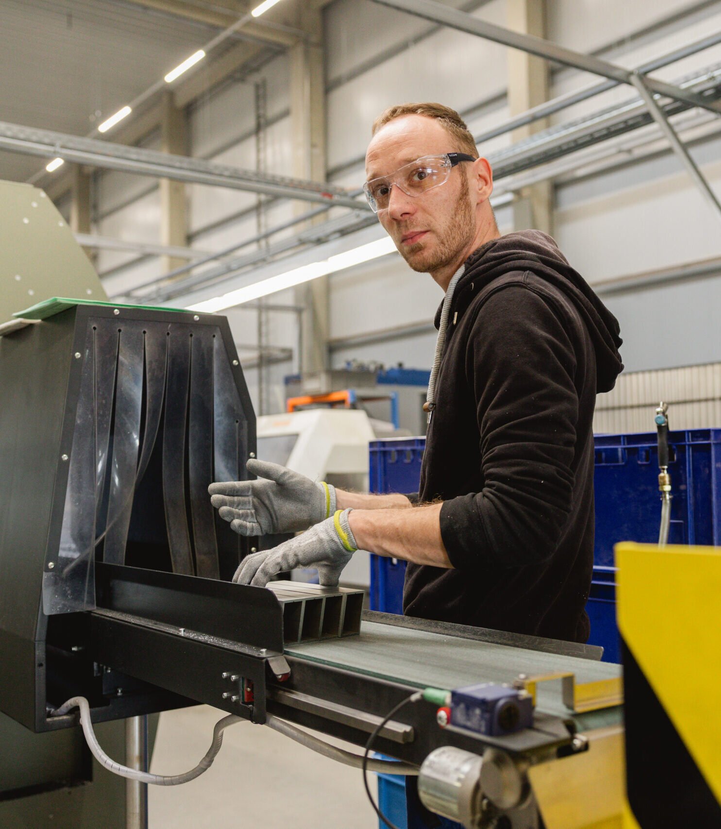 Ein Mann mit Schutzbrille und Handschuhen bedient eine Industriemaschine in einer Fertigungshalle.