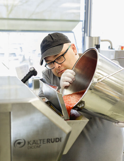 Ein Mann gießt rote Masse aus einem Stahltopf in eine Eismaschine.