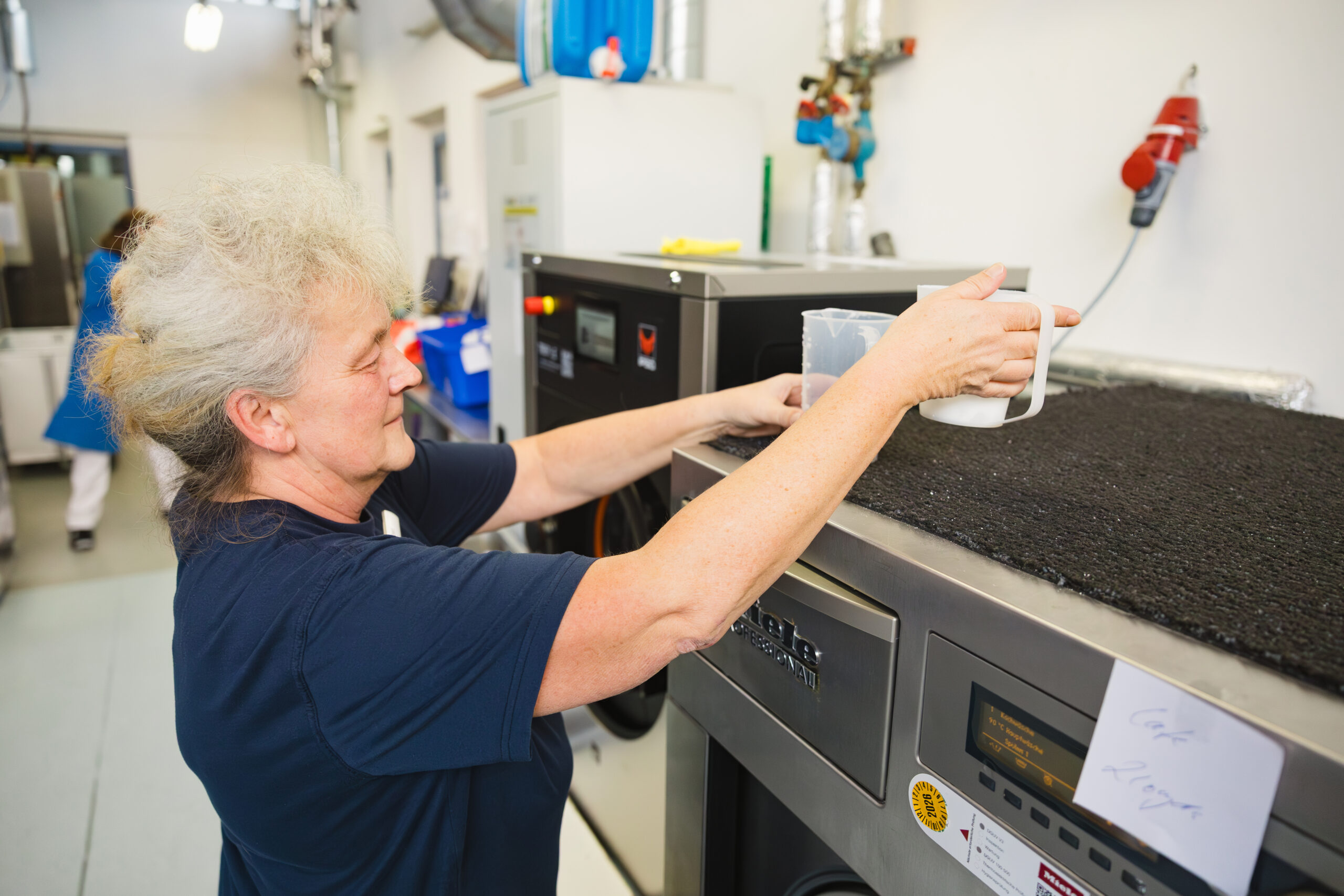 Eine Frau füllt Waschmittel in den Behälter einer Industriewaschmaschine.
