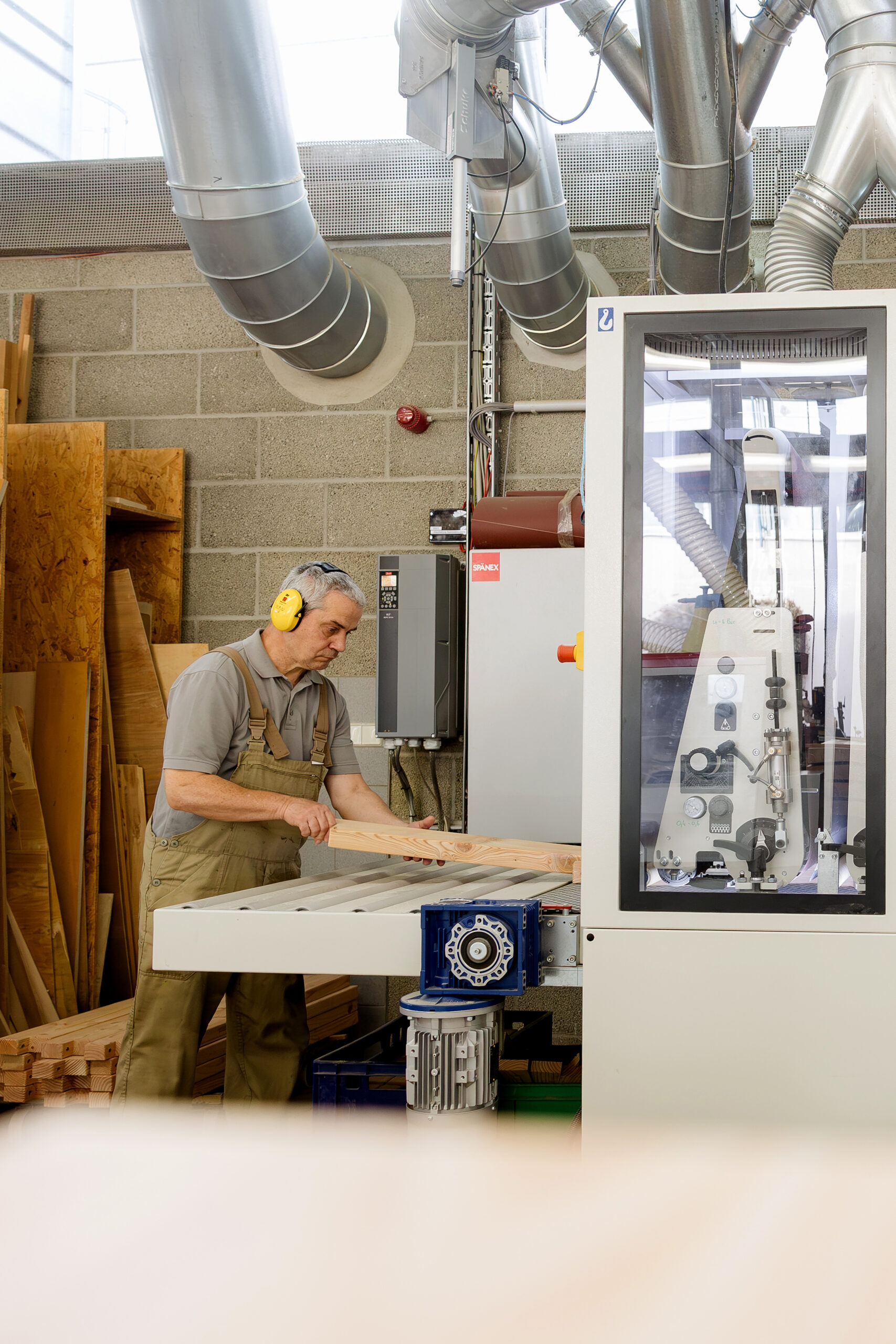 Ein Mann mit gelbem Gehörschutz und Latzhose schiebt ein Brett in eine Industriemaschine.
