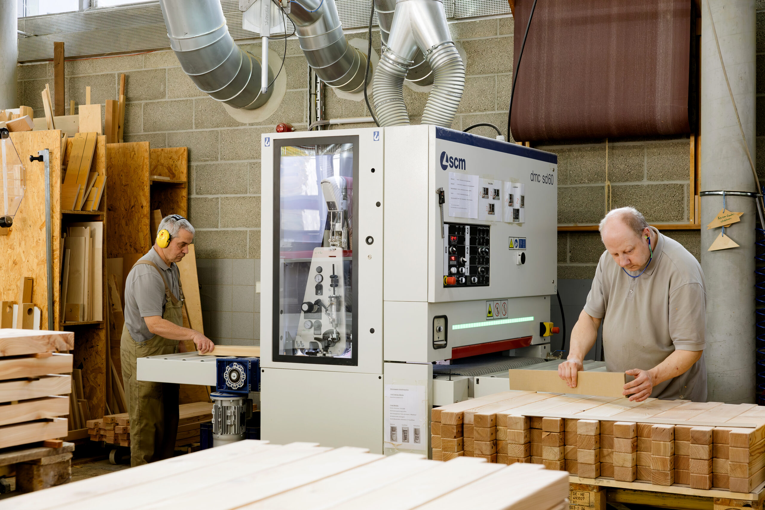 Zwei Männer arbeiten in einer Schreinerei an einer großen Holzbearbeitungsmaschine.