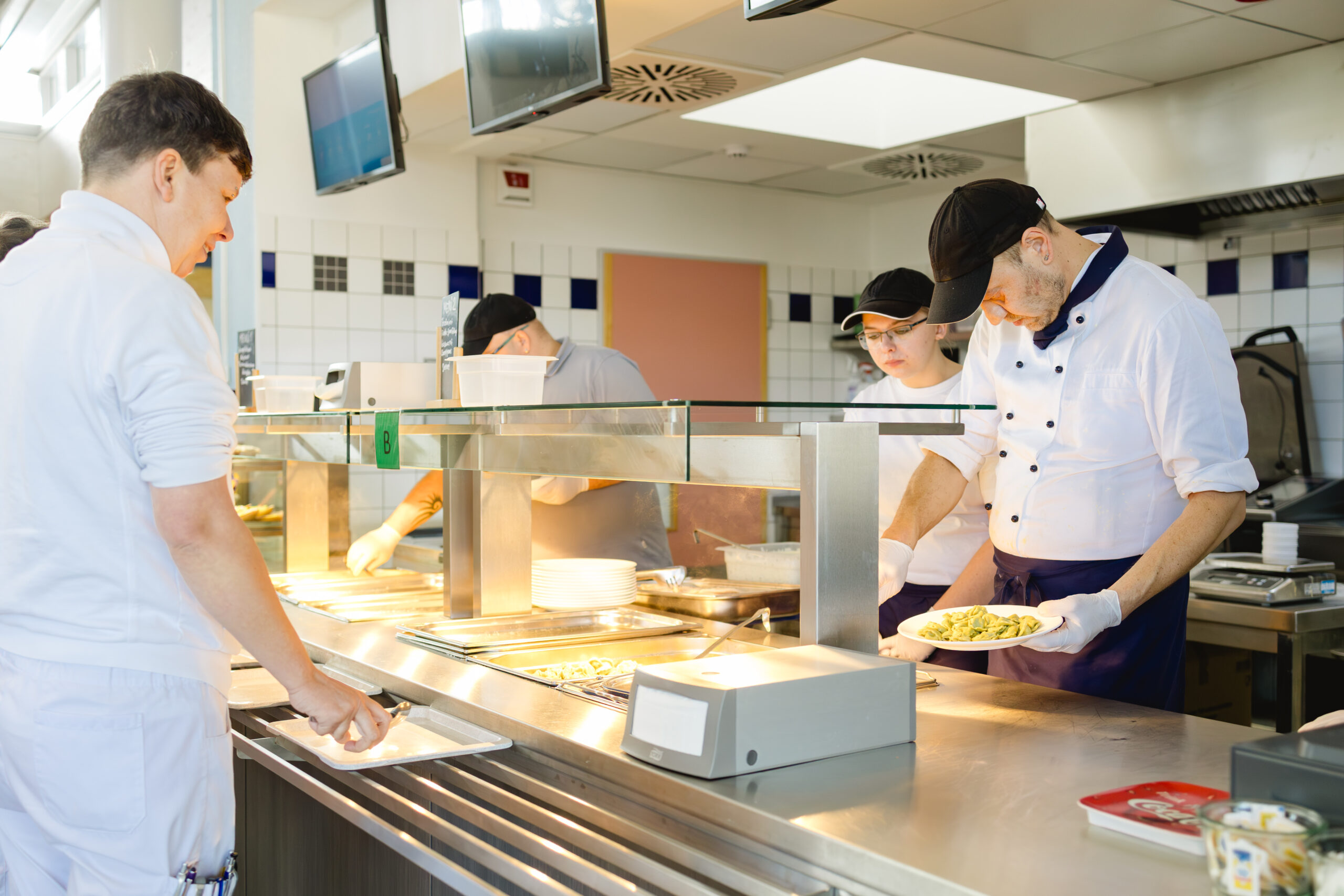 Drei Personen arbeiten gemeinsam an der Essensausgabe in einer Kantine.