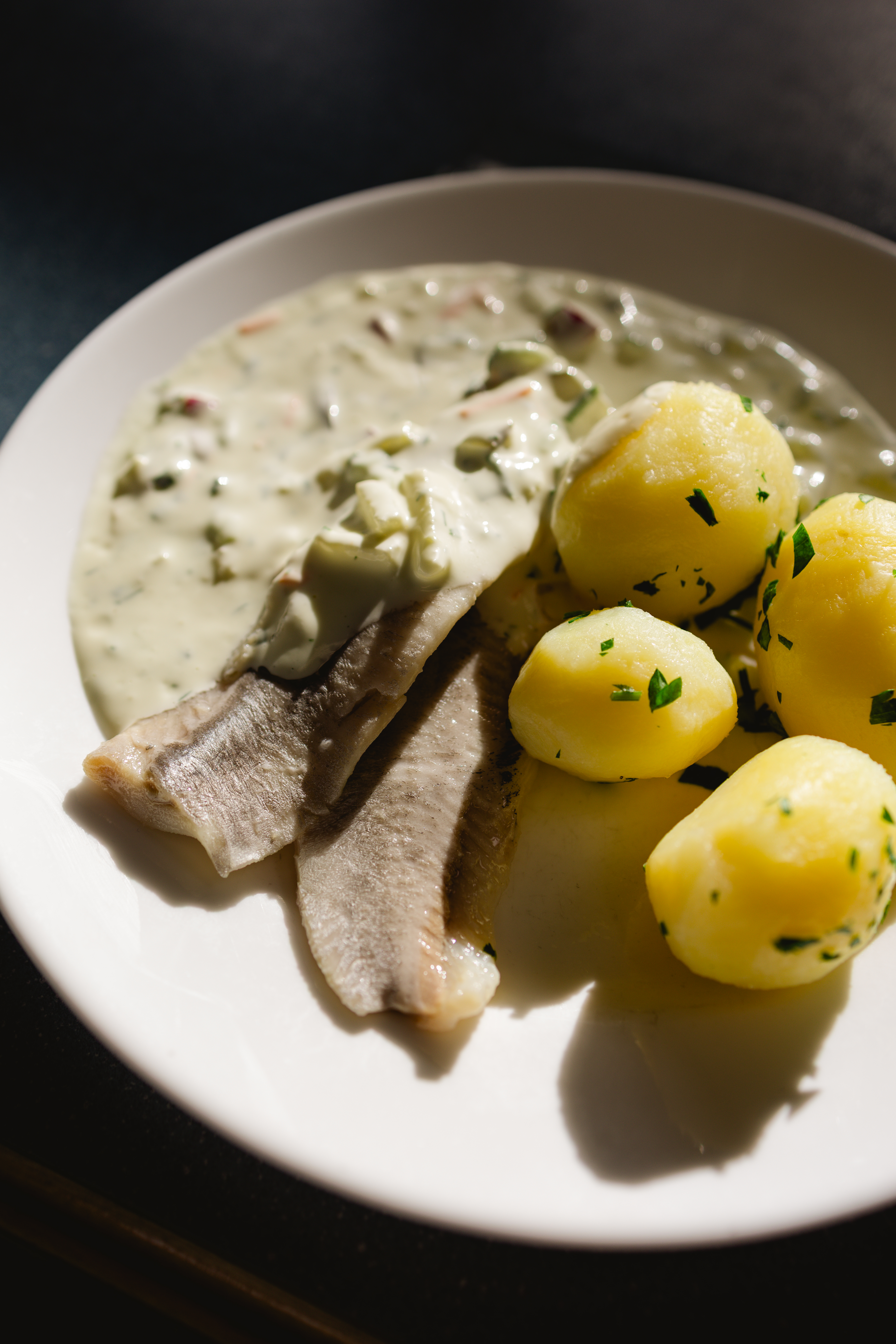 Ein weißer Teller mit Fischfilet, Kräutersauce und Salzkartoffeln.