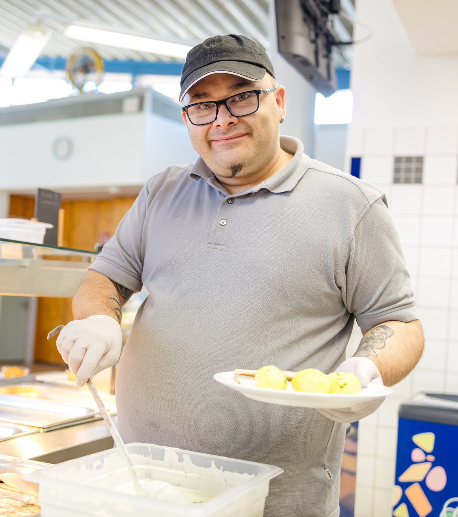 Ein Mann mit Brille und Schirmmütze hält einen Teller mit Kartoffeln an der Essensausgabe und lächelt.